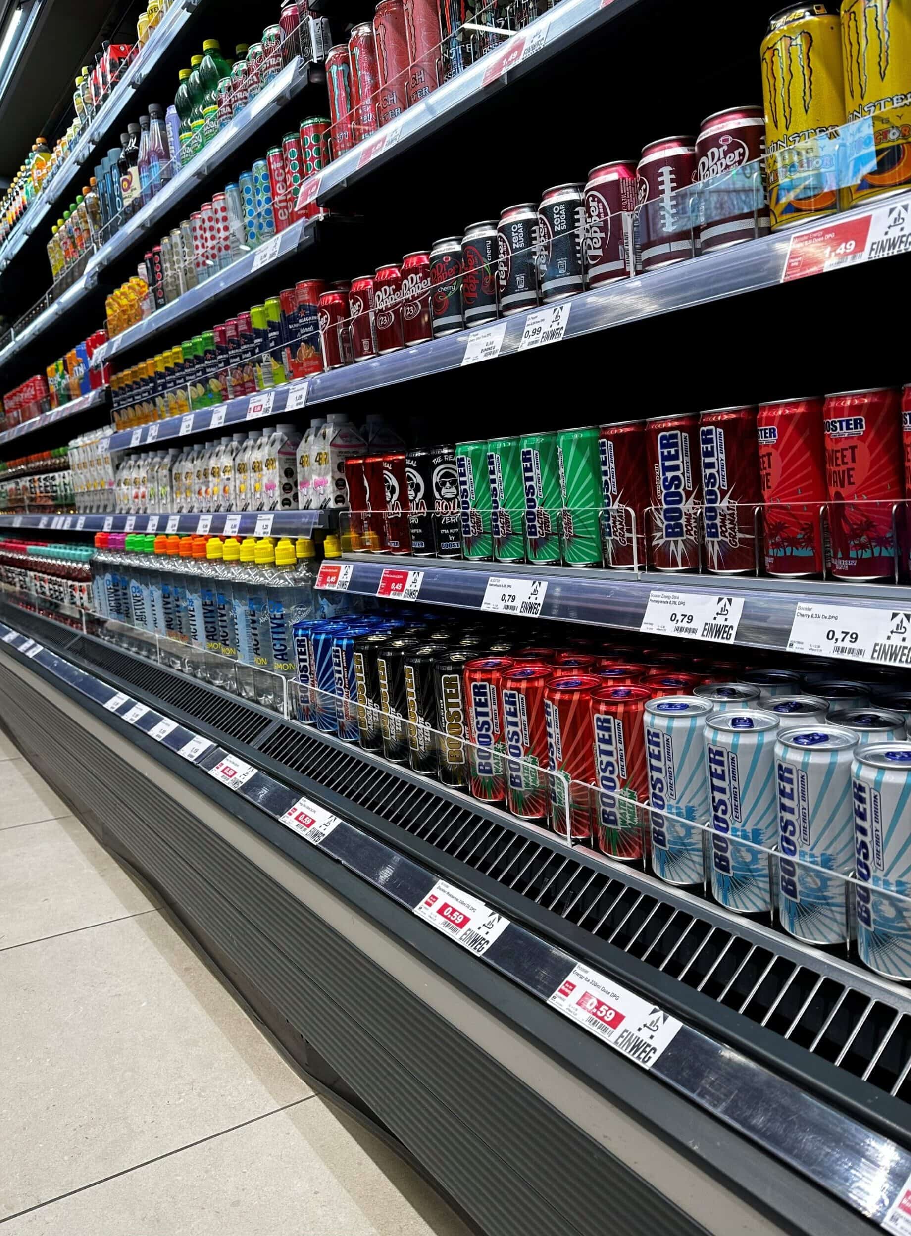 Cans frisdrank en bruisend drankje geselecteerd op Apotheek Kassa, drankregal in supermarkt, grote collectie frisdrank, kombucha en energiedrank, kleurrijk en aantrekkelijk gepresenteerd.