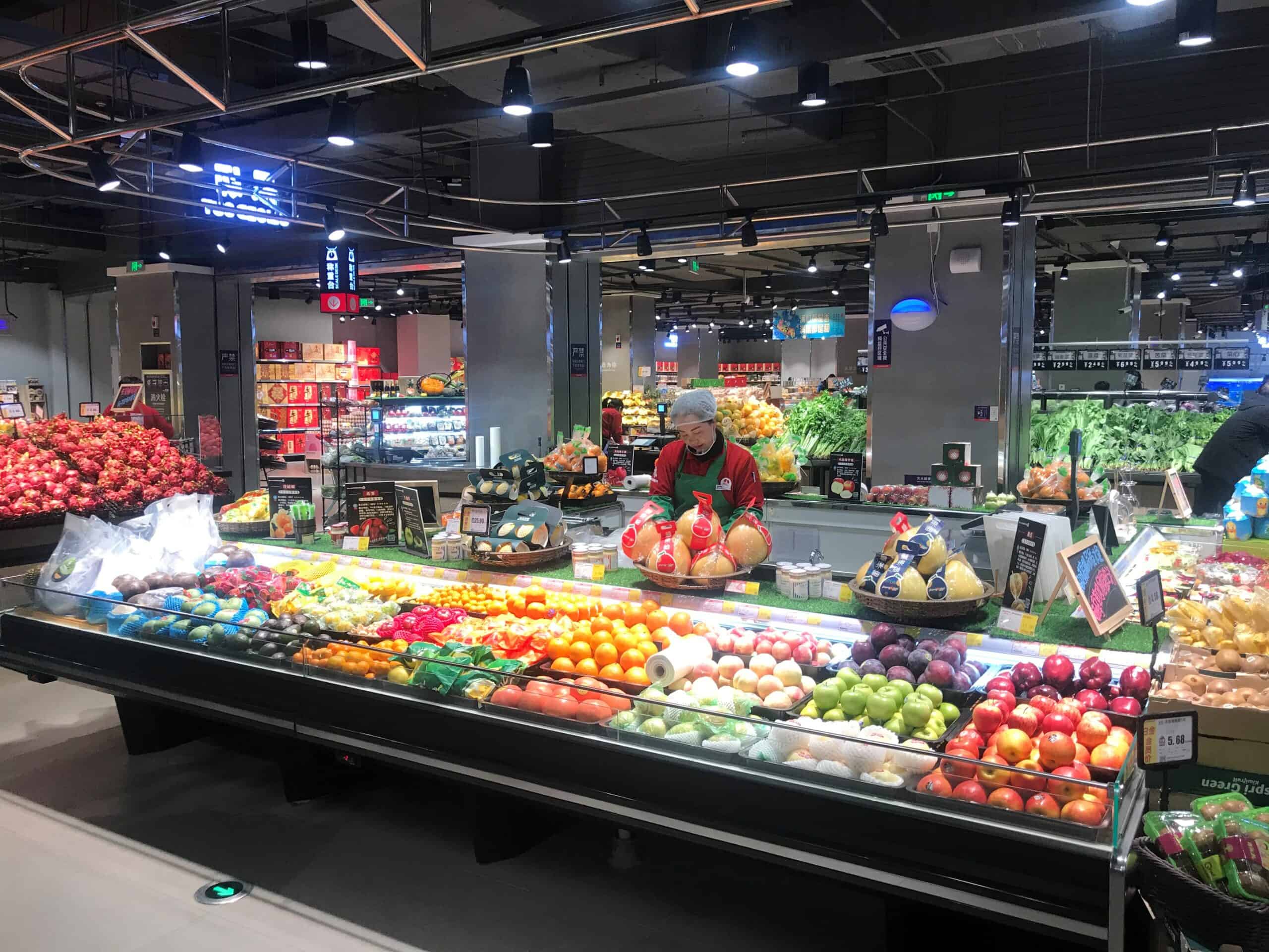 Vers gesneden fruit en groenten in een supermarktdisplay, verzorgd door Elips Solutions, met een medewerker die het fruit tussen de kleurrijke producten plaatst, ideaal voor verse en gezonde voedingsproducten.
