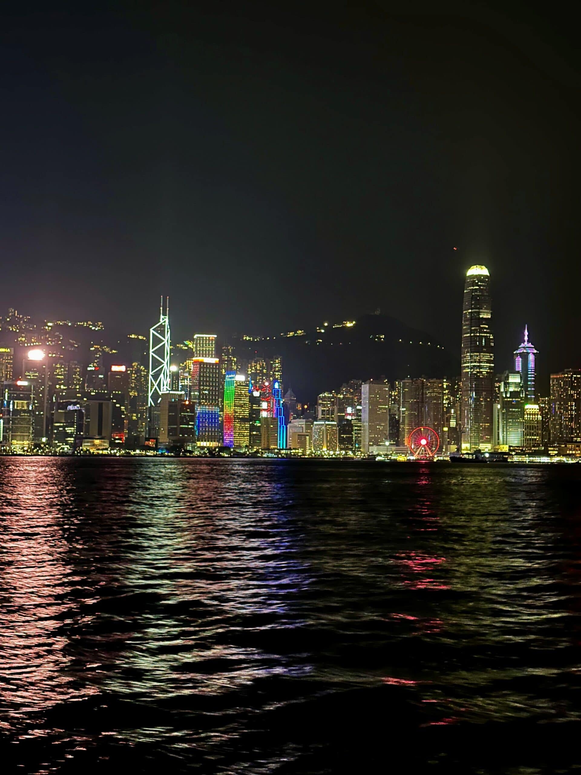 Modern verlichte skyline van Hong Kong bij nacht, reflektie op de waterkant met kleurrijke stadslichten en wolkenkrabbers.