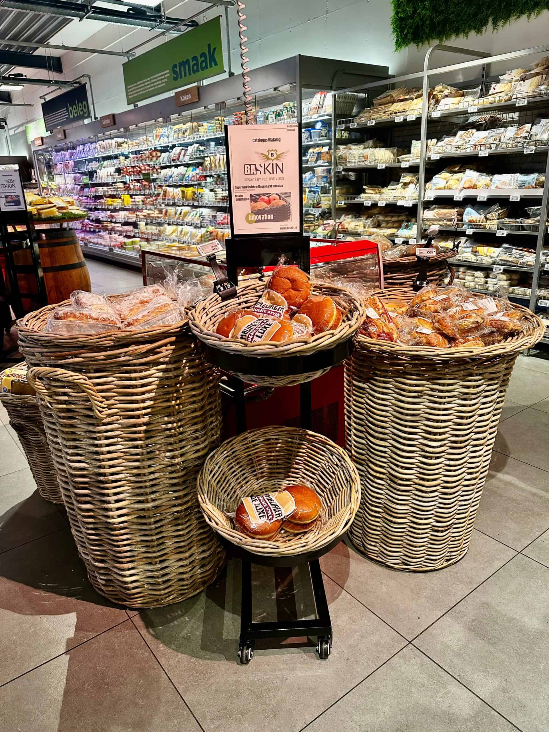 Versgebakken brood en zachte bollen in rieten manden bij supermarkt Elips Solutions, klaar voor aankoop, met grote gekoelde voedingsafdeling op de achtergrond.
