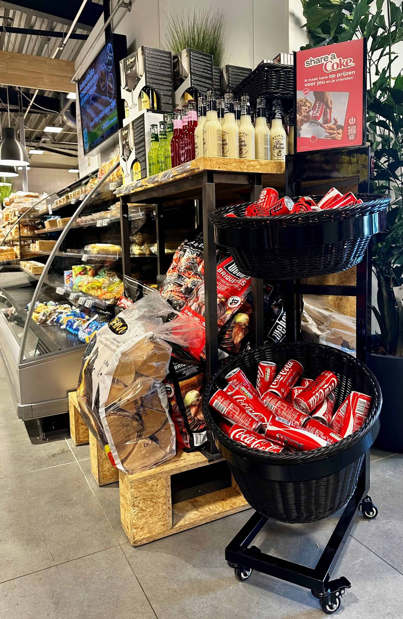 Kleine display met Coca-Cola blikjes en snacks in supermarkt, aantrekkelijke aanbieding en verscheidenheid aan frisdranken en snacks, geschikt voor promotie of klantbeleving.