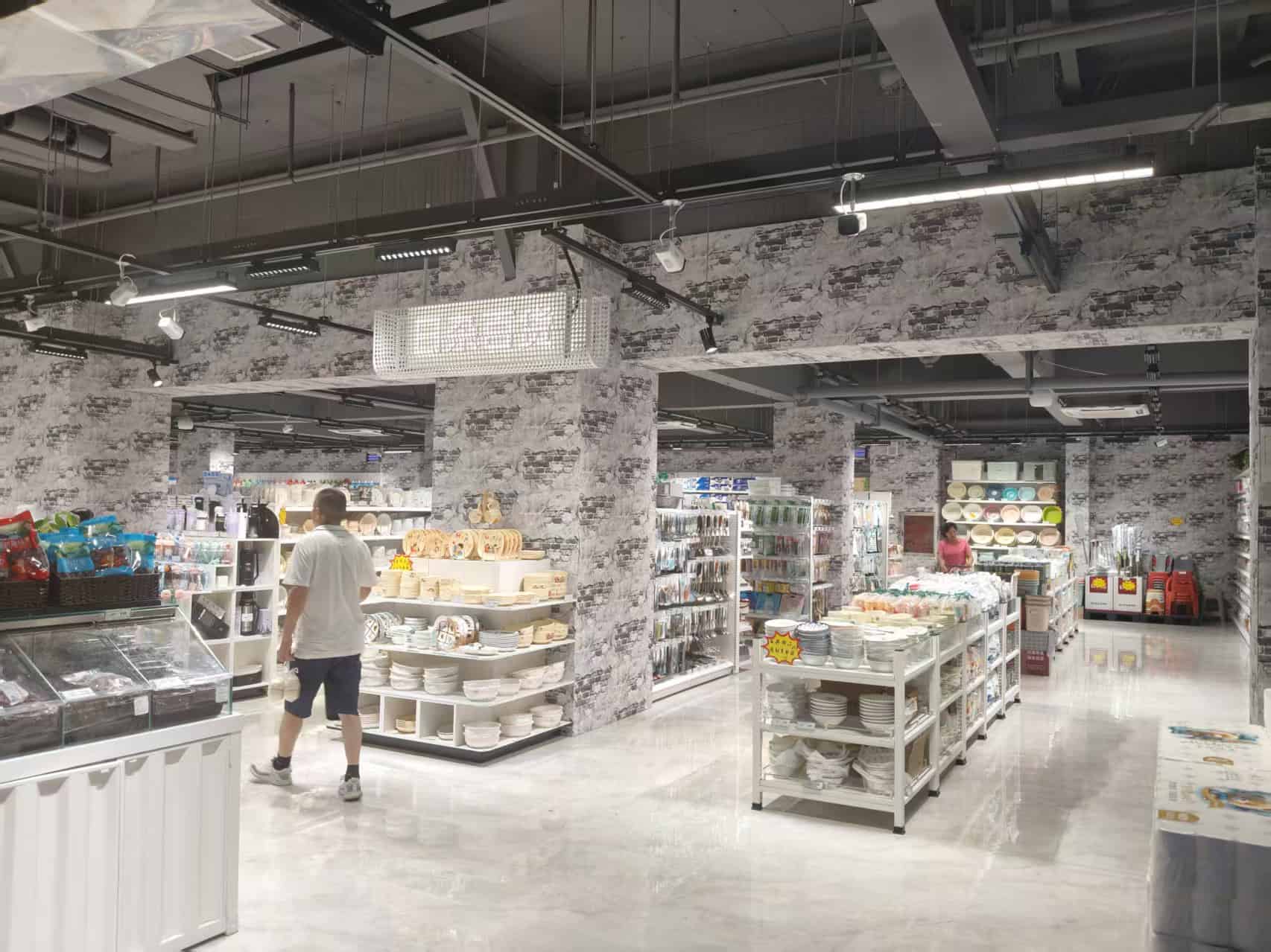 Kleine supermarkt met diverse keukengerei en servies, ingericht met industriële look, open plafond en moderne verlichting. Ideaal voor het vinden van keukenproducten en huishoudartikelen.