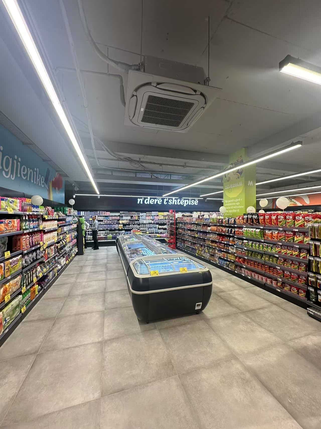 Koelvitrine in een supermarkt met brede gangpaden en schappen vol producten, verlichte plafondairconditioning en moderne verlichting, gericht op winkelbeleving, efficiëntie en klantservice.