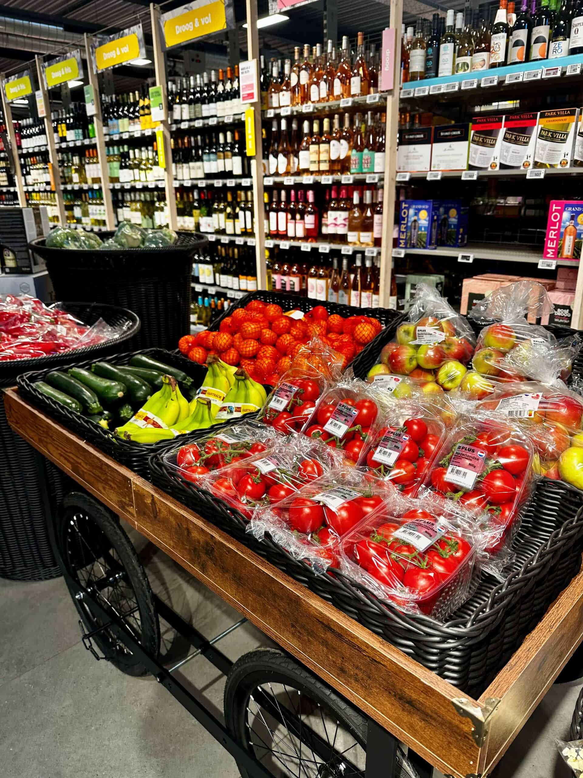 Rode tomaten, bananen, komkommers en citrusvruchten op een winkelkar in een supermarkt, met wijn en alcoholisch drinken op de achtergrond.