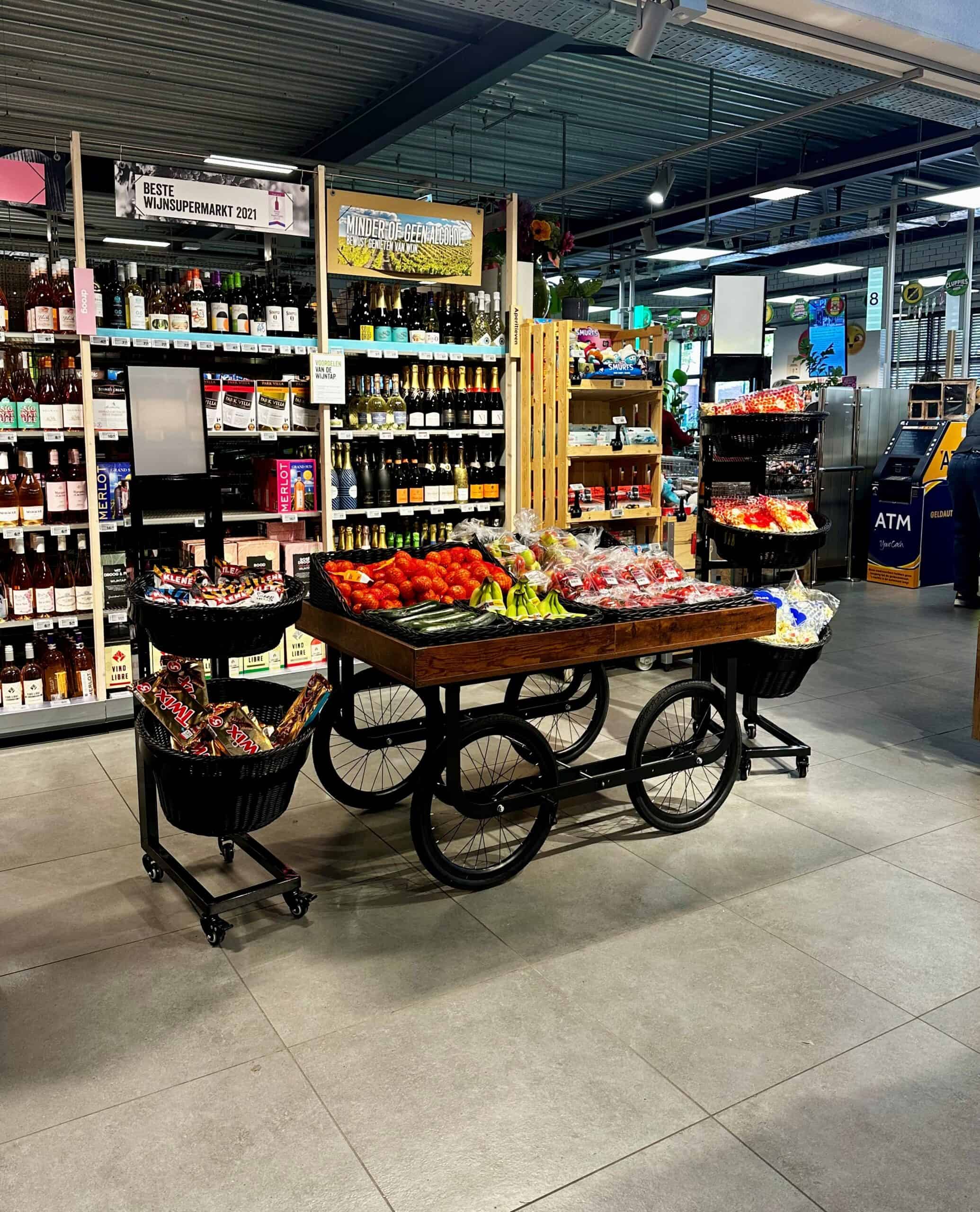 Kleurrige fruit- en groenteverspreiding in een supermarkt met wijnafdeling op achtergrond, benadrukt versheid en assortiment.
