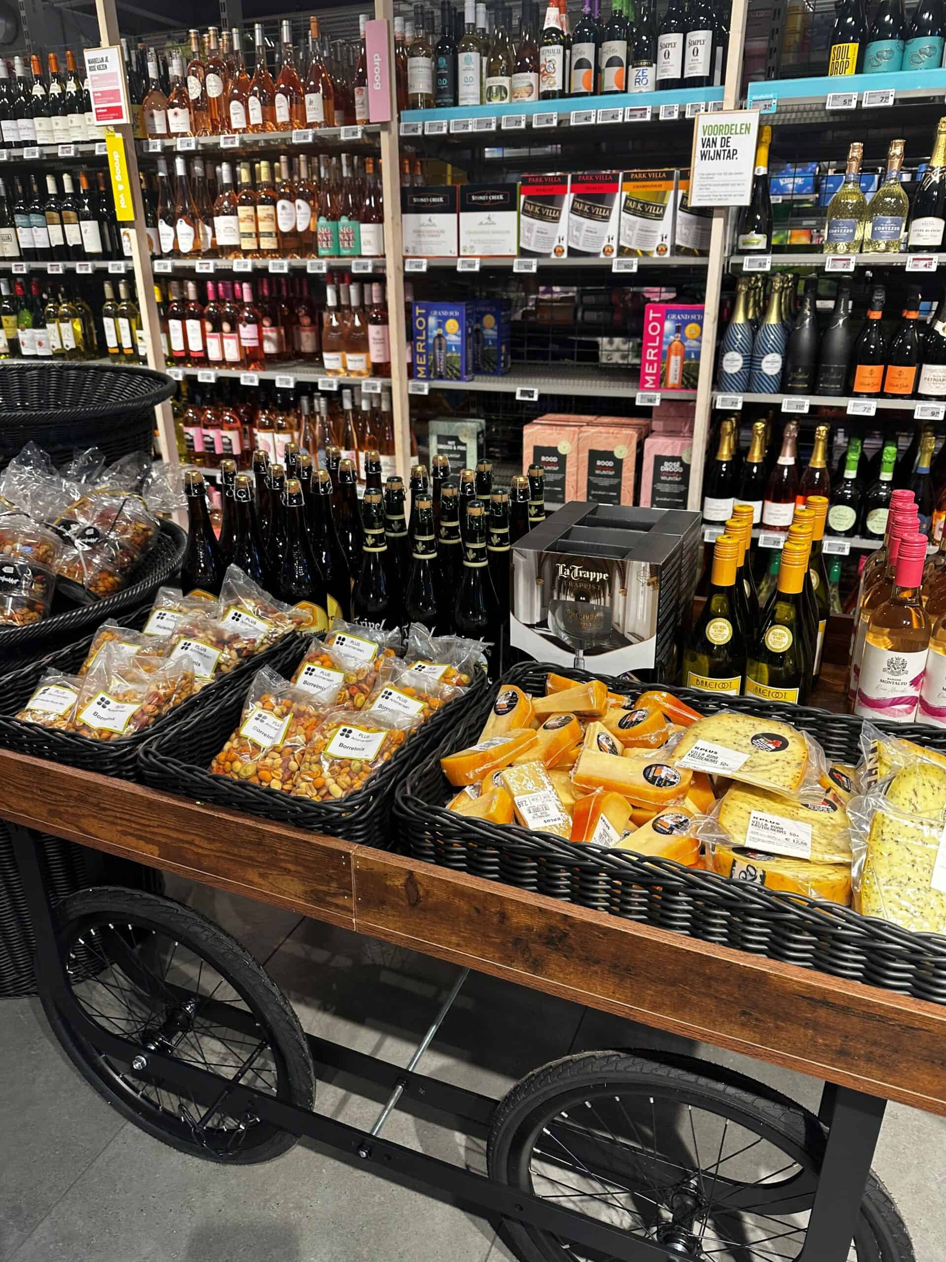 Bredereeks essentials van wijn, kaas en snacks op een winkelwagen in een supermarkt. Ideal voor wijnliefhebbers en kaasliefhebbers, perfect om te kopen in een deli of supermarkt voor een borrelplank.