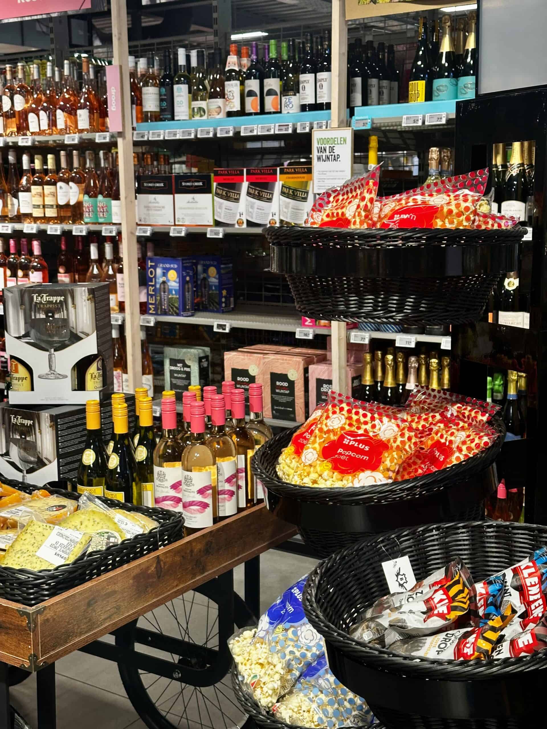 Popcorn en snackproducten in een winkel, naast wijn en alcoholische dranken, geserveerd in zwarte manden, met een winkelrek op de achtergrond, ideaal voor promotie of winkelindeling | Elips Solutions.