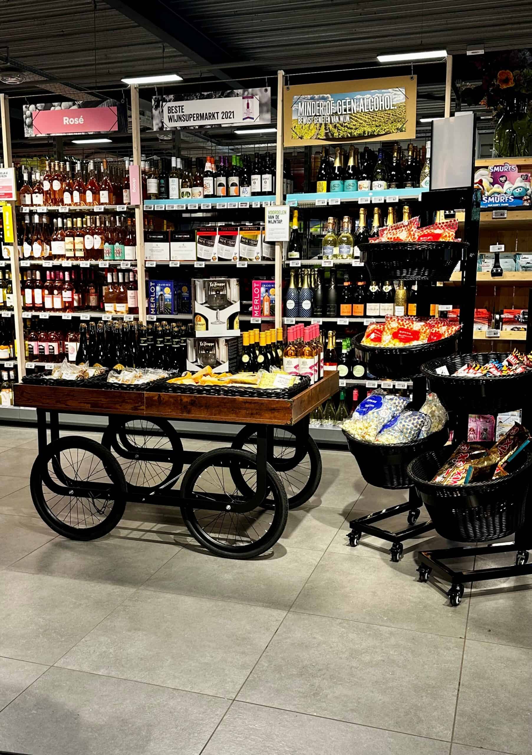 Alt: Winkel in een supermarktwinkel met wijn, snacks en shoppingwagens, klaar voor klanten, met duidelijke productindeling en promotieborden in een moderne winkelomgeving.