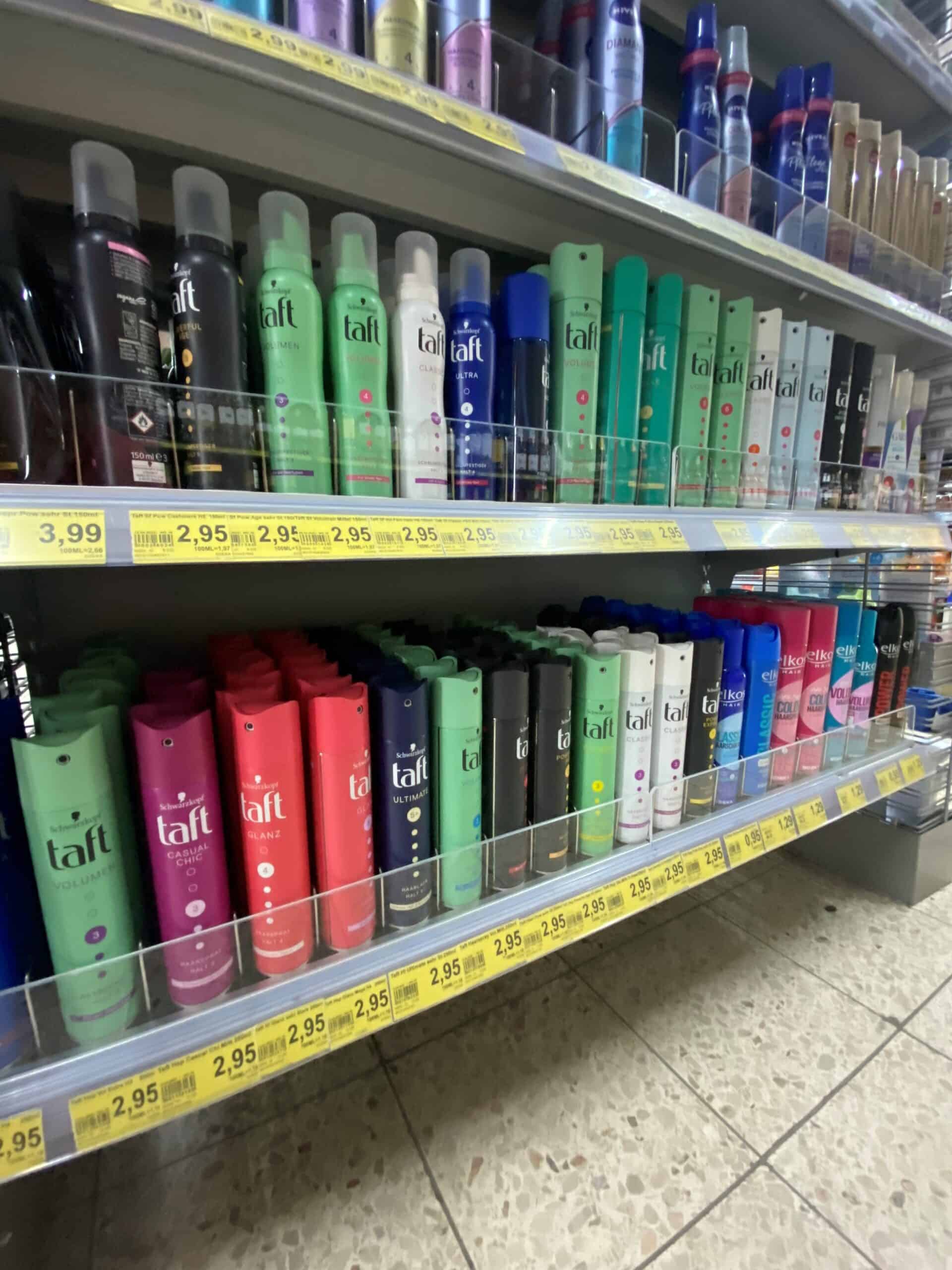 Sprays en haarverzorgingsproducten op een winkelrek bij een apotheek of supermarkt, gericht op haarverzorging en styling.