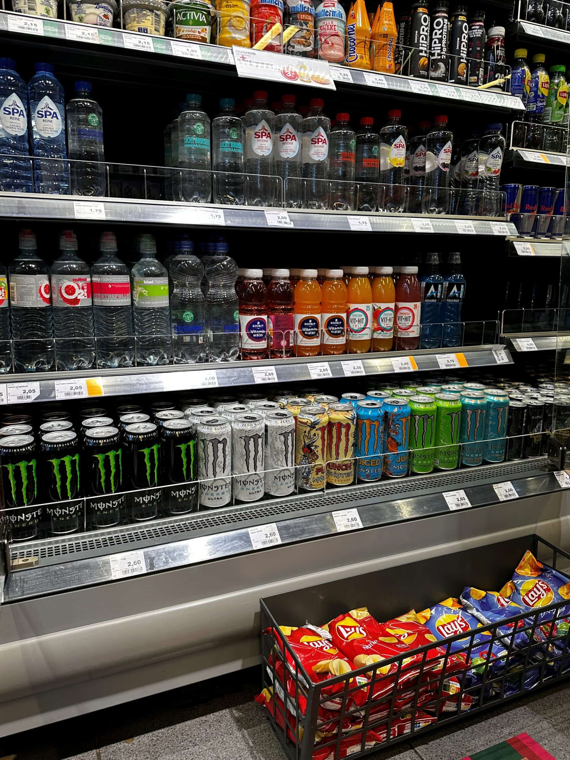 Schermafbeelding van een supermarktgang met diverse frisdrank- en watermerken op de schappen.