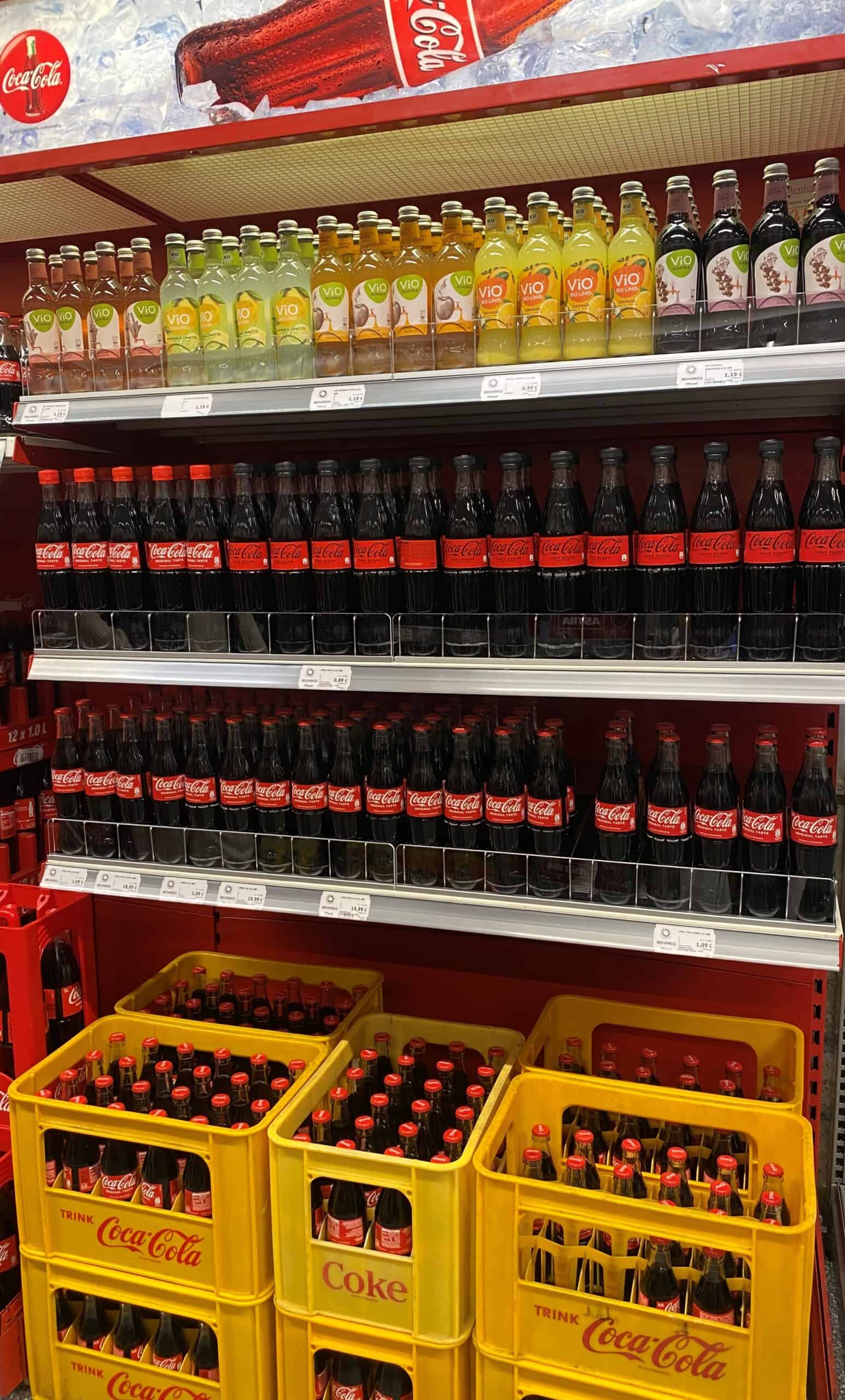 Coca-Cola en verschillende frisdrankflessen op een supermarktplank, voor een verfrissende drankkeuze.