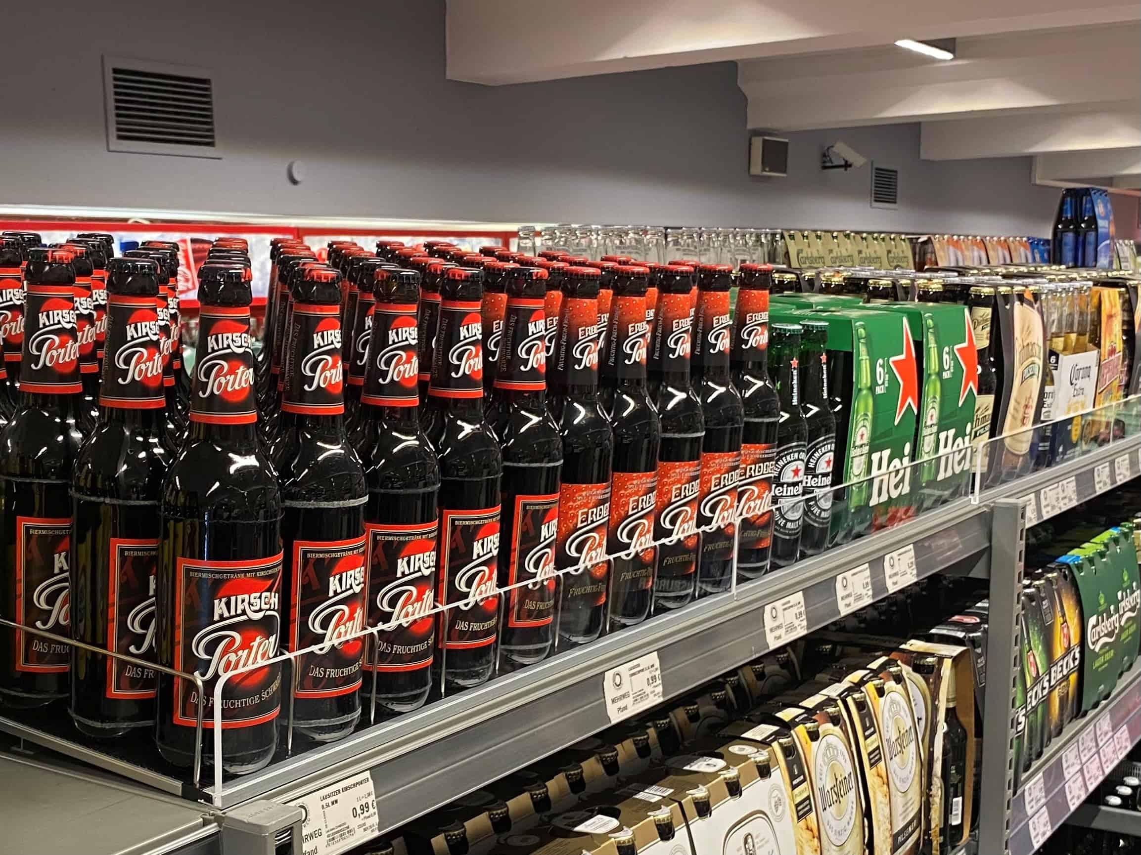 Heineken bierpakken en andere frisdranken op supermarktrek, presentatie van alcoholische dranken en blikjes in winkel, uitgebreide selectie van populaire drankmerken, verkoopdisplay in detailhandel.