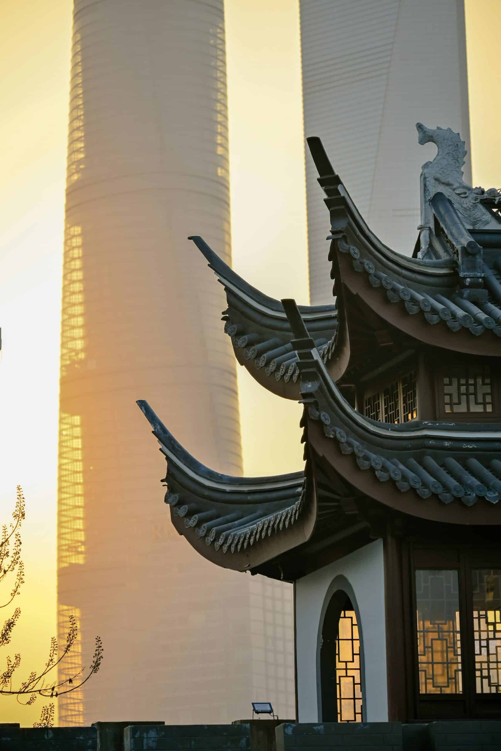 Elegante traditionele Chinese pagode met moderne wolkenkrabbers op de achtergrond, sfeervol verlicht tijdens zonsondergang.