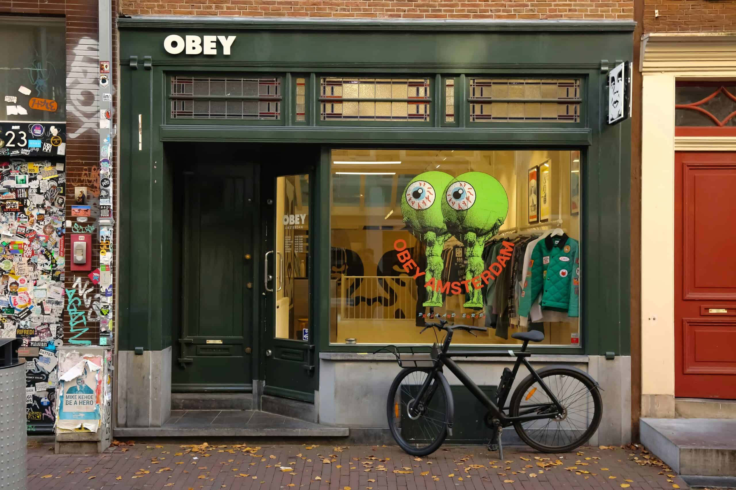 Bruggen van het Elips Solutions kantoor met opvallende cartoon-achtige groene oogpoppen in het raam die Amsterdam vertegenwoordigen, fiets voor de ingang en een muur vol stickers.