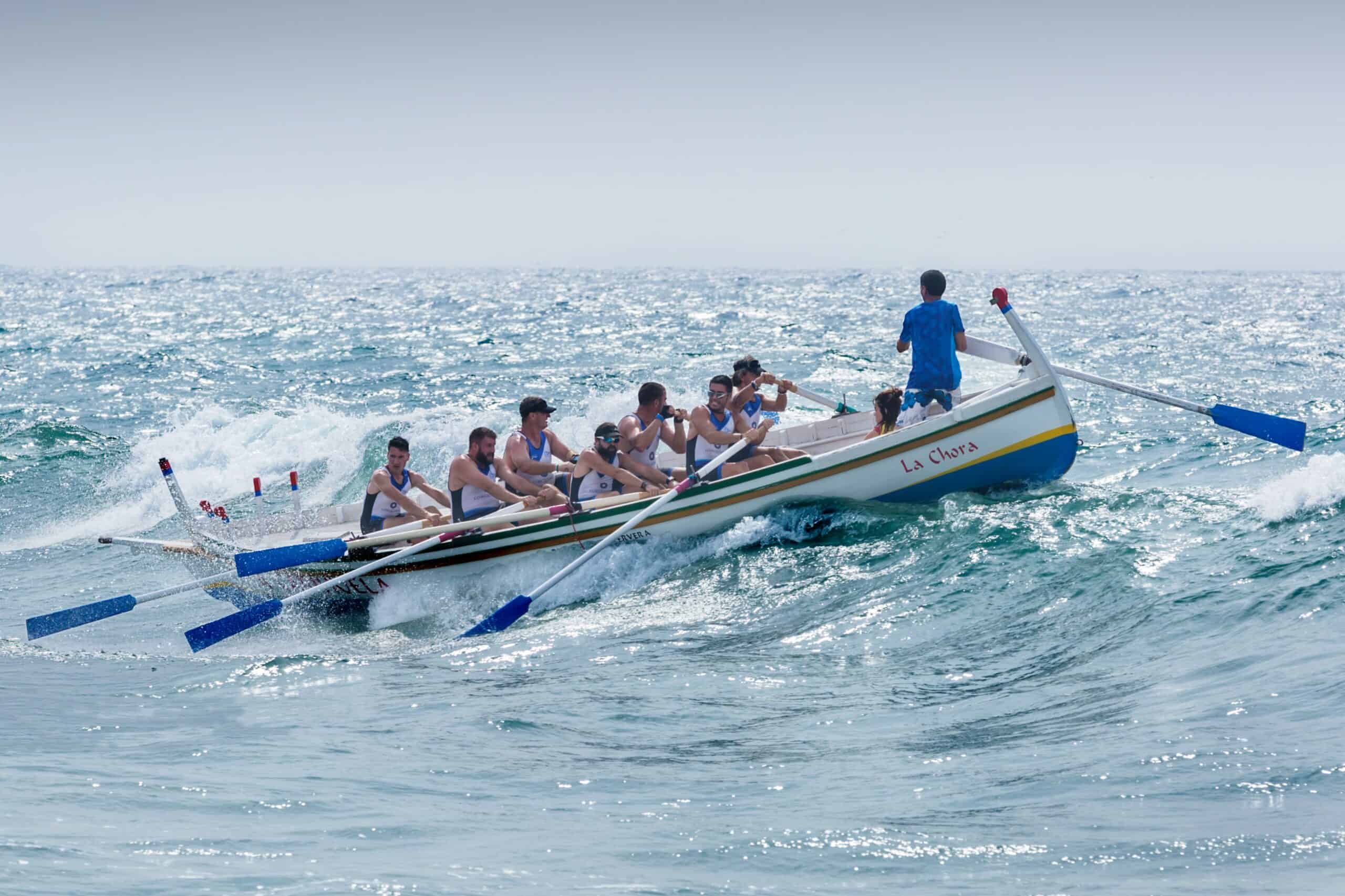 Roeiboot vol team te water, teamgeest en zeilenwedstrijd, sportieve watersport, zomerse boottocht, Elips Solutions, strategisch teamwerk op zee.