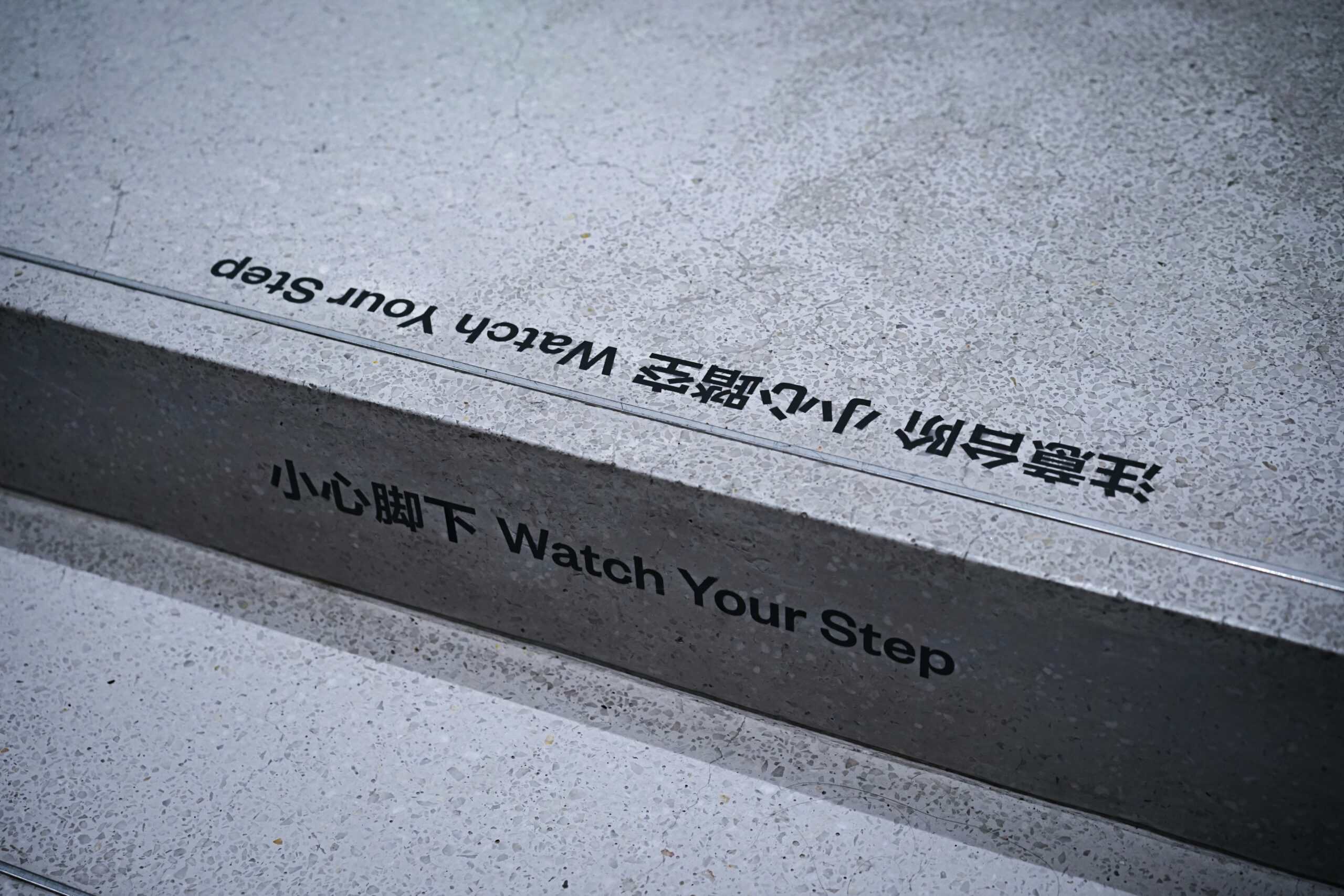 Veiligheidssignaal op trap met tekst: "Watch Your Step" en Chinese karakters, benadrukt het belang van veiligheidswaarschuwingen op werkplekken en openbare plaatsen.